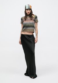 Multi-colored cropped knit top with zigzag pattern, paired with a black satin maxi skirt. Model wears a patterned silk scarf.