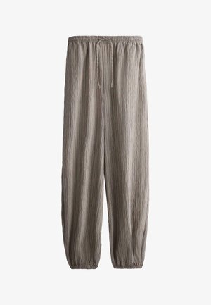 Voľné béžové nohavice s elastickým pásom, sťahovacou šnúrkou vpredu, textúrovanou látkou a elastickými manžetami na členkoch.