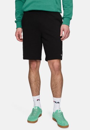 Black cotton shorts with a relaxed fit, featuring an embroidered FILA logo. Paired with green suede sneakers and white socks.