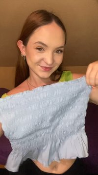 Top corto smock azul claro con dobladillo con volantes, que presenta un tejido texturado con líneas horizontales. El material parece suave y elástico.