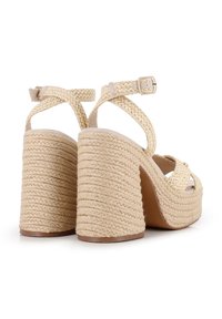 Sandalias de plataforma beige con una textura trenzada, que presentan un tacón grueso de cuerda trenzada y una correa en el tobillo con una hebilla metálica.