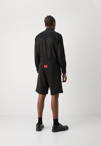 Veste noire surdimensionnée avec short assorti, dotés d'une taille élastique, d'une couleur unie, et d'un détail de marque rouge au dos.