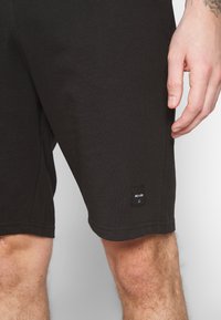 Shorts de algodón negros con un diseño recto, costuras laterales y una pequeña etiqueta de la marca cerca del dobladillo. Textura suave con un ajuste elástico.