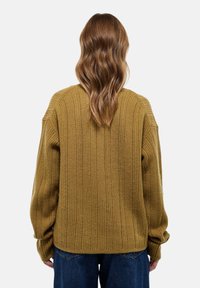 Pull en ribbed moutarde avec une coupe décontractée, des manches longues et des épaules tombantes. Présente un tricot texturé et un ourlet droit.