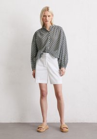 Blusa con motivo, maniche lunghe e frontale annodato, abbinata a pantaloni corti bianchi e sandali in tessuto color nocciola. Tessuto testurizzato e vestibilità rilassata.