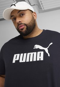 Marineblauwe katoenen T-shirt met een groot wit 'PUMA'-logo en een witte pet met een zwart PUMA-logo. Eenvoudig ontwerp, korte mouwen.