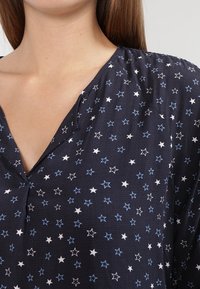 Blusa navy con un motivo a stella bianco e azzurro chiaro, con scollatura a V e tessuto testurizzato. Design casual con maniche corte.