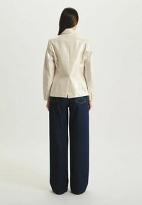 Blazer métallique clair à la coupe ajustée et aux revers en pointe, associé à un jean en denim foncé à jambes larges avec des coutures contrastées.