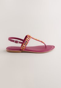 Sandale plate rose avec bride de cheville ajustable et détails perlés jaunes, orange et blancs sur la bride en T, semelle beige et entre-doigt arrondi.