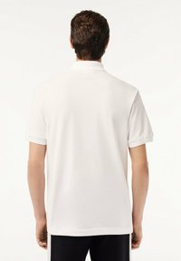 Camisa polo blanca hecha de tela suave, con mangas cortas y cuello doblado. Textura lisa con un corte relajado.