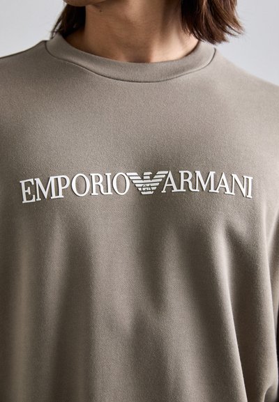 Szürke pamut pulóver kerek nyakkal. A mellkason fehér "Emporio Armani" felirat és logó található. Puha, sima tapintású.