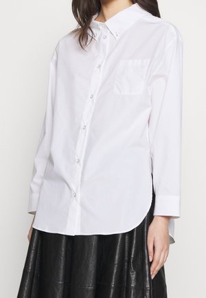 Chemise blanche à boutons en coton lisse, dotée d’un col pointu, de manches longues et d’une poche poitrine. Ourlet arrondi avec une coupe décontractée.