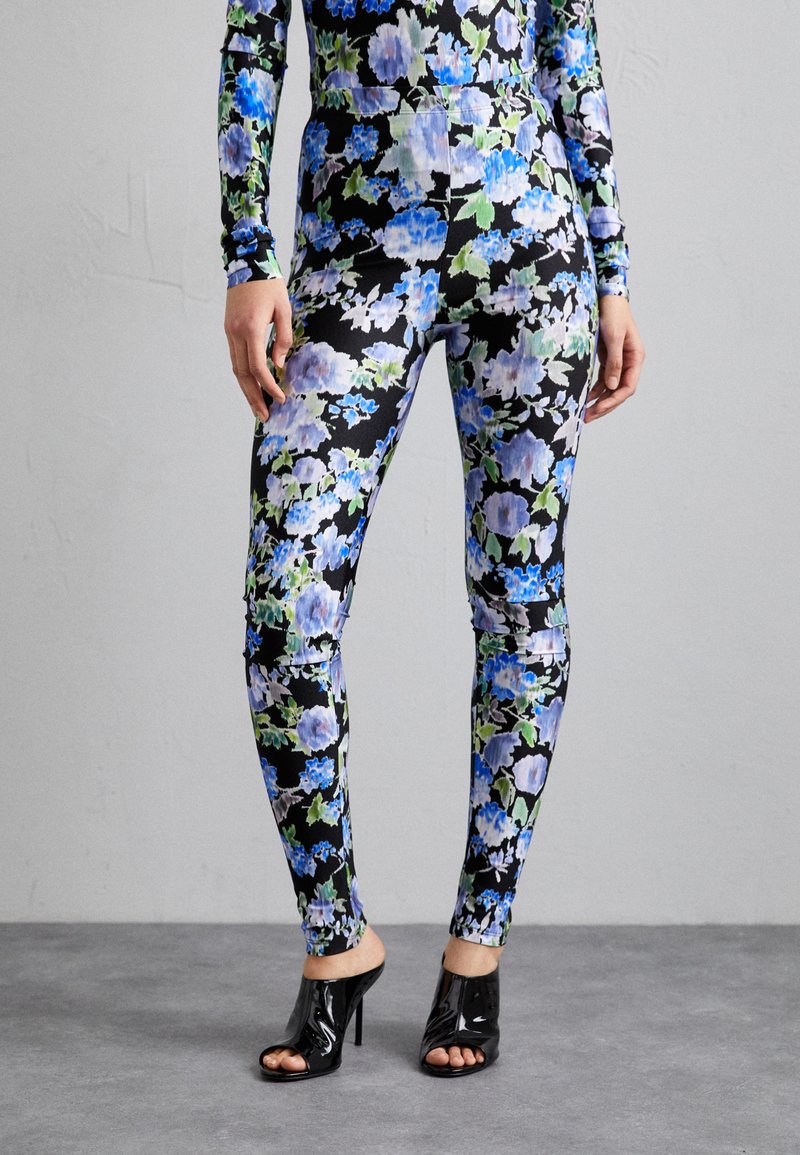 Floral leggings in black with blue and green patterns, fitted design, stretchy material, paired with open-toe heeled shoes.