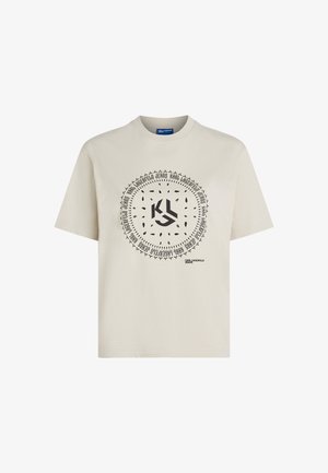 Bež majica iz 100% bombaža s kružnim crnim grafičkim dizajnom koji uključuje tekst i motive lišća, kratki rukavi i okrugli izrez.