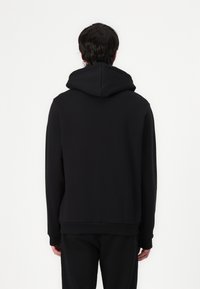 Sudadera negra con capucha de corte relajado, puños y dobladillo acanalados, textura suave y diseño sencillo, vista desde la parte de atrás.