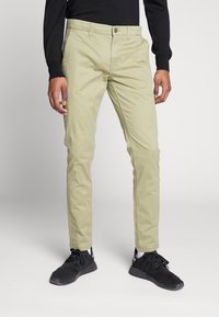 Light green cotton pants with a slim fit, featuring a button and zip closure, side pockets, and a smooth texture. Worn with black sneakers.
