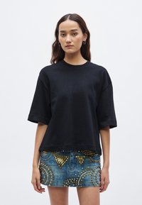 Čierne oversized bavlnené tričko s krátkymi rukávmi, skombinované s džínsovou minisukňou ozdobenou kovovými nitmi a kruhovým vzorom.