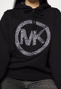 Black hoodie with a large circular graphic featuring the letters "MK" in a gray leopard print. Includes a drawstring hood and soft texture.
