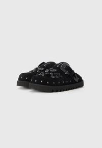 Pantofi negri slip-on cu talpă groasă, cu ținte decorative din metal și catarame mari, pe un fundal alb.