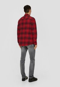Rode en zwarte geruite flanellen shirt met een knoopkraag, lange mouwen en een relaxte pasvorm, gecombineerd met grijze jeans en zwarte schoenen.