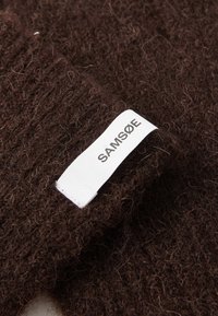 Brown knitted sweater detail, featuring a soft, fuzzy texture. White label with "SAMSØE" in black letters attached to the fabric.