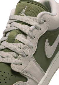 Zielono-szary tenisówka z teksturowanego zamszu i siateczkowych materiałów. Posiada białe sznurowadła i logo Nike w kształcie łyżwy. Detale przeszyć i perforowany przód.