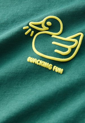 T-shirt en coton vert avec un motif brodé d'un canard jaune et le texte "QUACKING FUN" dans une police ludique, présentant une texture lisse.