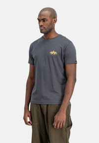 Hall gray puuvillane T-särk ümmarguse kaeluse, lühikeste varrukate ja kollase graafilise disainiga rindkeres. Varrukal on silt.