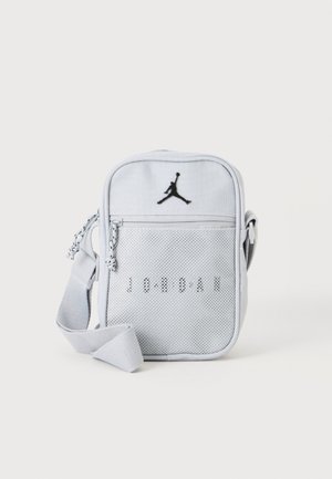 Mała jasnoszara torba na ramię z przednią siateczkową kieszenią, czarnym logo Jumpman i regulowanym paskiem na białym tle.