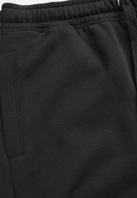 Svarta mjukisbyxor i mjukt tyg med resår i midjan och sidfickor, med slät textur och minimal detaljering.