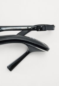 Svarte lakkhøyhælte sandaler med tynn ankelselle, spiss tå og glansfull finish. Har stiletthæler og spenne.