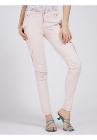 Lichtroze slim-fit cargobroek met zijzakken, een gladde textuur en zichtbare stiksels. Gecombineerd met blauwe sandaaltjes met hakken en banden.