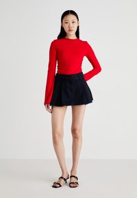 Haut rouge à manches longues au design ajusté, associé à une mini-jupe noire évasée avec des bords effilochés. Des sandales noires à talons complètent la tenue.