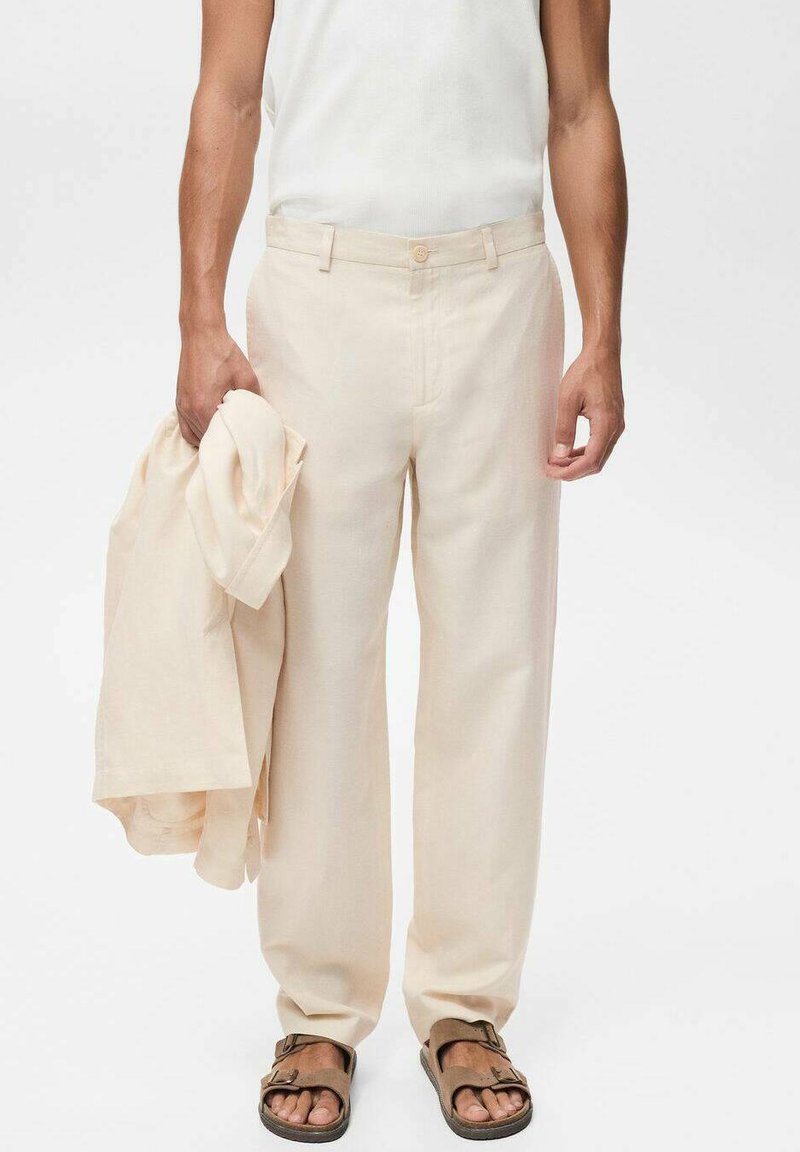 Beige Leinenhose mit lockerer Passform, ausgestattet mit einem Knopfverschluss und Seitentaschen, gehalten neben einem passenden Hemd. Braune Sandalen getragen.