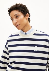 Sudadera a rayas en crema y azul marino, con cuello redondo y tejido texturizado, y un logo bordado en el lado izquierdo del pecho.