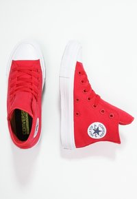 Sneaker alte in tela rossa con punta e suola in gomma bianca, dotate di lacci e di una toppa con logo sul lato esterno.