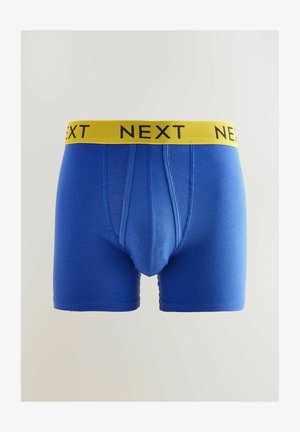 Mėlyni apatiniai šortai, pagaminti iš medvilnės mišinio, su geltona elastinga juosta, ant kurios juodu raštu užrašyta "NEXT". Lygus paviršius ir prigludęs dizainas.