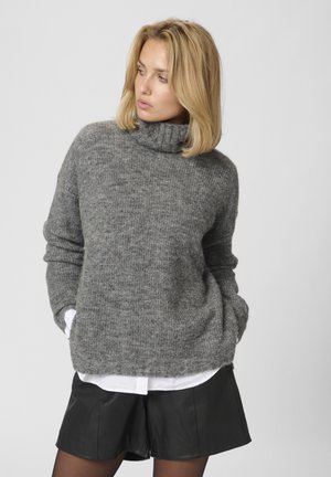 Gray knitted turtleneck sweater with a loose fit, paired with black leather shorts. The sweater features a textured finish and ribbed collar.