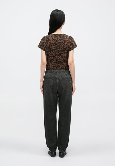 Brązowa koszula w cętki lamparta z krótkim rękawem i okrągłym dekoltem, zestawiona z luźnymi, ciemnoszarymi jeansami, elastycznymi mankietami i tylnymi kieszeniami.