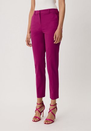 Femme portant un pantalon slim couleur magenta, longueur cheville, assorti à des sandales à talons hauts fines et un haut blanc sans manches.
