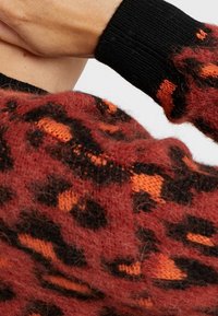 Oversized trui in gerookt rood en zwart met oranje luipaardprint, voorzien van zwarte geribbelde manchetten en een pluizige afwerking.