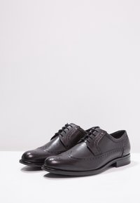 Chaussures habillées en cuir noir avec design à bout golf, décorations de broguages, bout rond et lacets. Finition lisse avec un aspect poli.