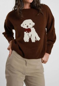 Maglione di maglia marrone con motivo di un cane bianco con un fiocco rosso sul davanti. Il design presenta maniche ampie e un collo a costine.