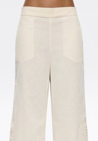 Linnen broek in lichtbeige met een wijde pijp ontwerp. Voorzien van zijzakken en uitgebreide borduursels op de lagere randen.