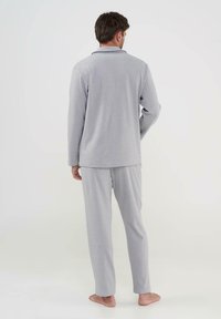 Conjunto de pijama gris con una parte superior de manga larga y pantalones, que presenta una sutil textura en la tela y ribetes negros en el cuello, mostrado desde la parte de atrás.