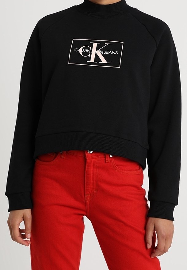 Sweat-shirt court noir avec logo Calvin Klein Jeans blanc, associé à un pantalon taille haute rouge vif.