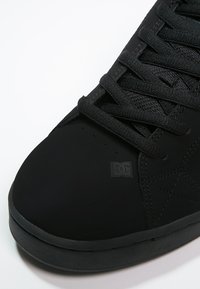 Sort skate sko med en glat mat overflade, teksturerede snørebånd, subtil logodetalje og en rund tå, med en gummisål.