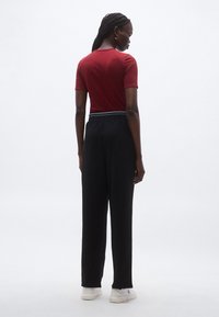 Czerwony top z krótkim rękawem i okrągłym dekoltem, w połączeniu z wysokim stanem czarnych spodni i białymi sportowymi butami, widziany od tyłu.