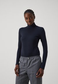 Dunkelblaues Langarm-Turtleneck-Oberteil aus dehnbarem Stoff, kombiniert mit leichten, grauen Cargo-Hosen mit elastischem Bund und Taschen.