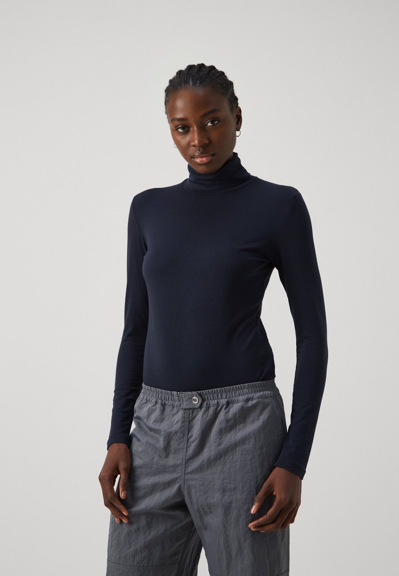 Dunkelblaues Langarm-Turtleneck-Oberteil aus dehnbarem Stoff, kombiniert mit leichten, grauen Cargo-Hosen mit elastischem Bund und Taschen.